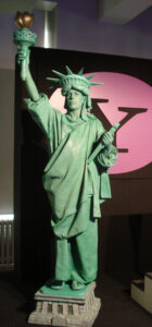A performer dressed and painted as the Statue of Liberty posing in its classic position, holding the torch above her head.