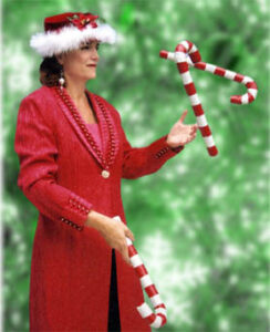 A juggler dressed in a long red coat juggling three large striped candy canes.