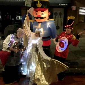 A group of event performers dressed in light up costumes as Snow King and Queen, and a toy soldier in front of an inflatable light-up nutcracker.