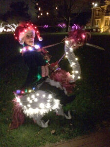 An event performer dressed as an elf decked out in holiday lights riding a large magical bird puppet.
