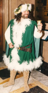A Christmas party entertainer dressed in a green and white Ghost of Christmas Present costume, holding a metal goblet.