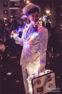 An actor dressed in an LED Jack Frost costume holding a light up wand and suitcase.