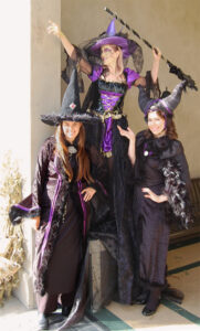 Three event performers pose together dressed in black and purple witch costumes.