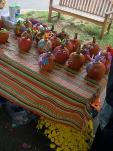 A table covered in decorated small pumpkins, decorated with marker and paint, as well as various craft supplies such as googly eyes, pipe cleaners and stickers.
